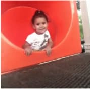 Una niña pequeña despidiendose y deslizandose por un tobogan.